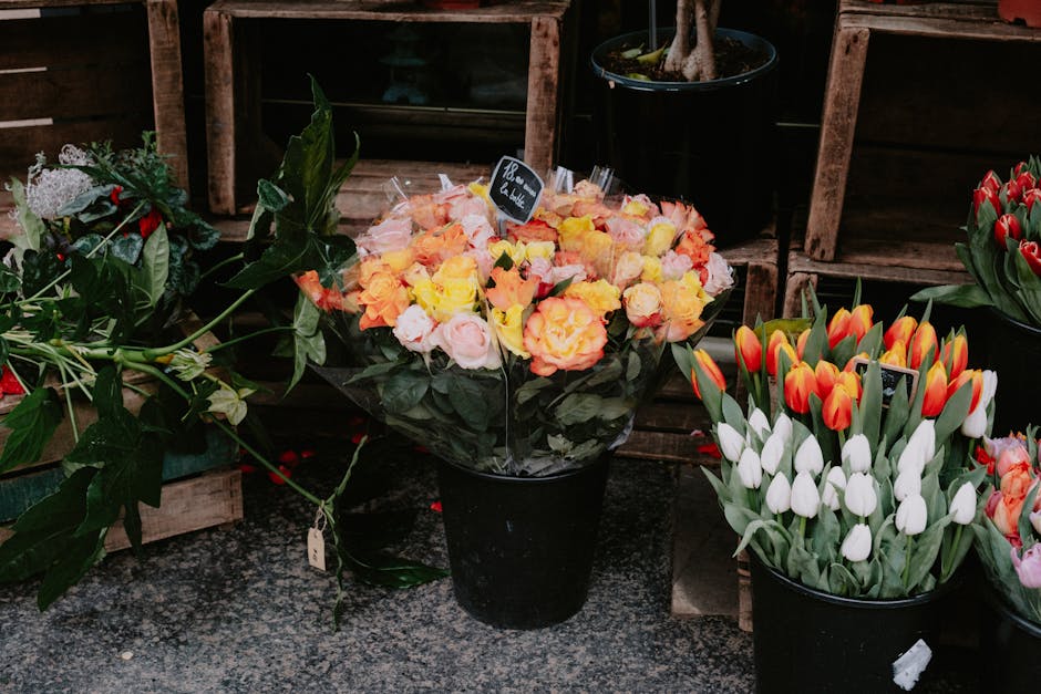 A black flowerpot containing a bouquet of fresh roses in shades of yellow, peach, and soft pink, with lush green leaves. The bouquet is arranged in a rounded, full style and displayed on a granite sur